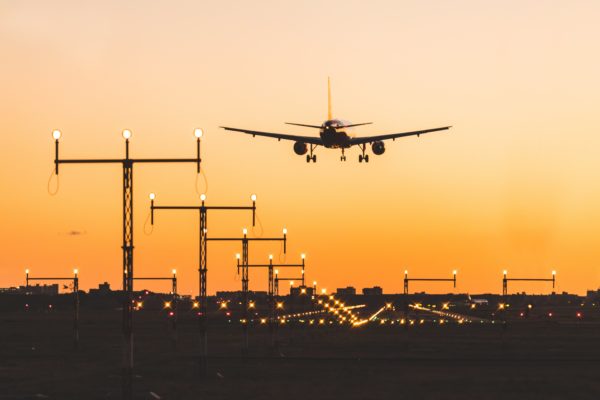 Plane landing with an orange sunset in the background and airfield lights